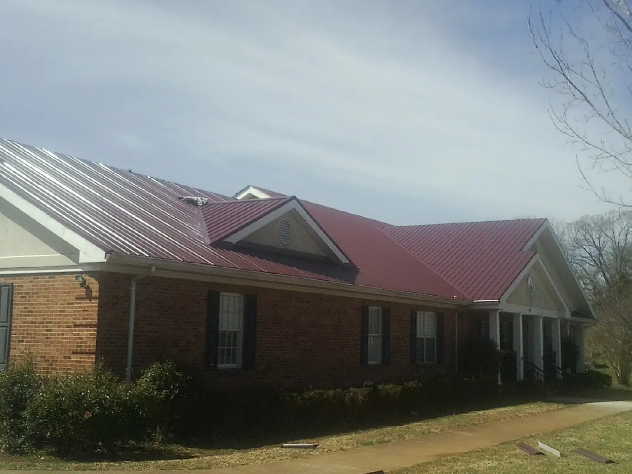 Red metal roof with gabled entries on a long brick building, from a Hail Damage Roof Repair job in Lakeview